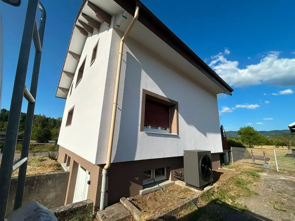 Maison individuelle après isolation par l'extérieur à Anould, unité extérieure de pompe à chaleur en pied de façade